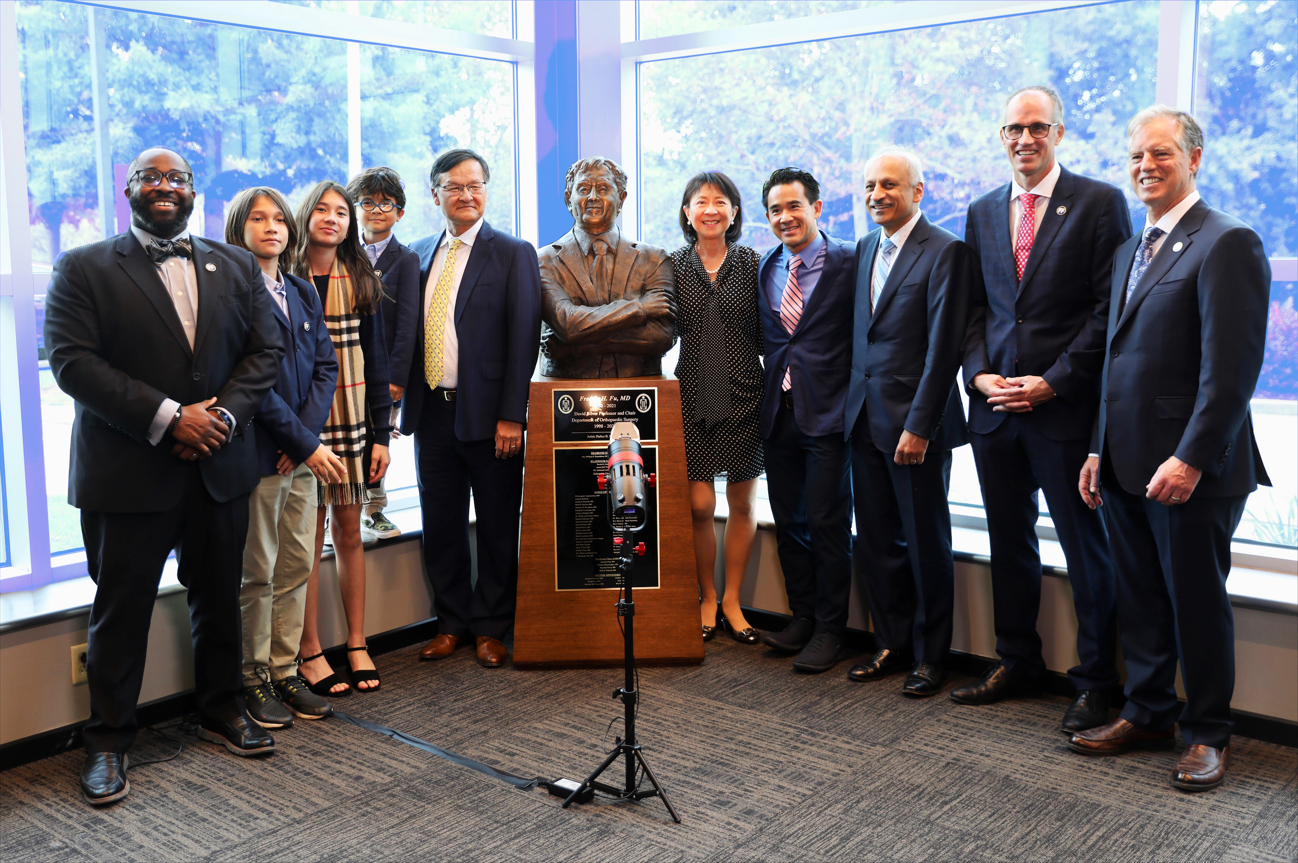 A group of smiling individuals with a bronze bust of Dr. Fu in the middle of them.